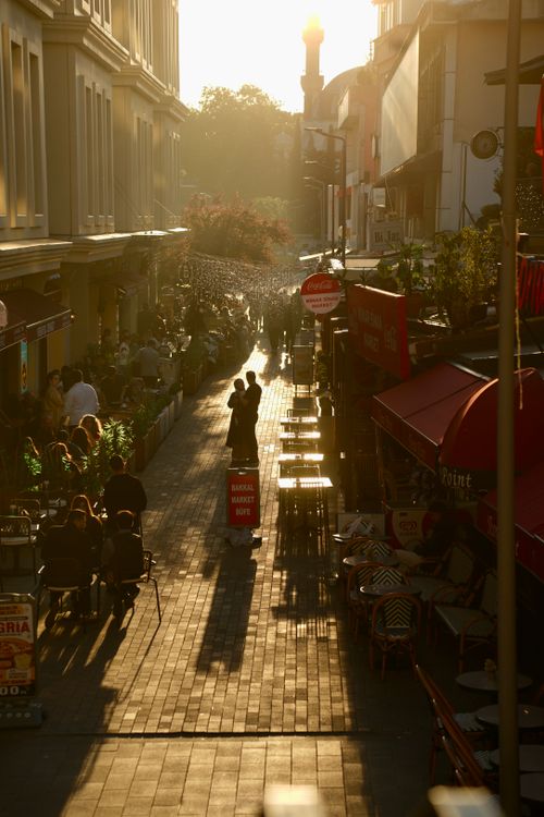 Free Sunlit urban street scene with bustling cafes and evening silhouettes. Stock Photo