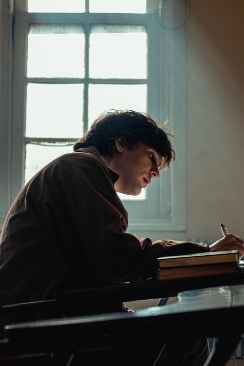 Free Silhouette of a young student writing in a classroom with sunlight streaming through the window. Stock Photo