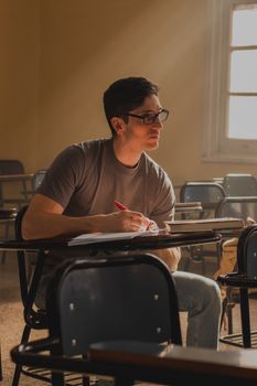 A young man attentively studies in a sunlit classroom, deep in thought.