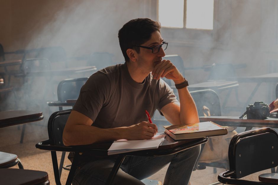 Thoughtful student sitting with a book in a sunlit, smoky classroom. Thoughtful student sitting with a book in a sunlit, smoky classroom.