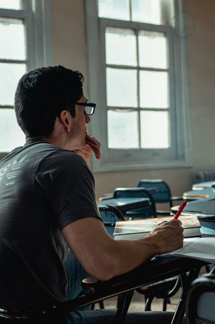 Male student in a classroom writing notes while studying alone. Quiet academic environment. Male student in a classroom writing notes while studying alone. Quiet academic environment.