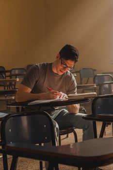 A young adult student intensely focused on studying in a dimly lit classroom.
