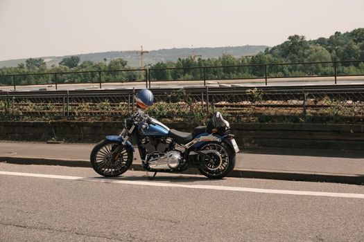 Parked blue cruiser motorcycle near a river with hills in the background on a clear day.