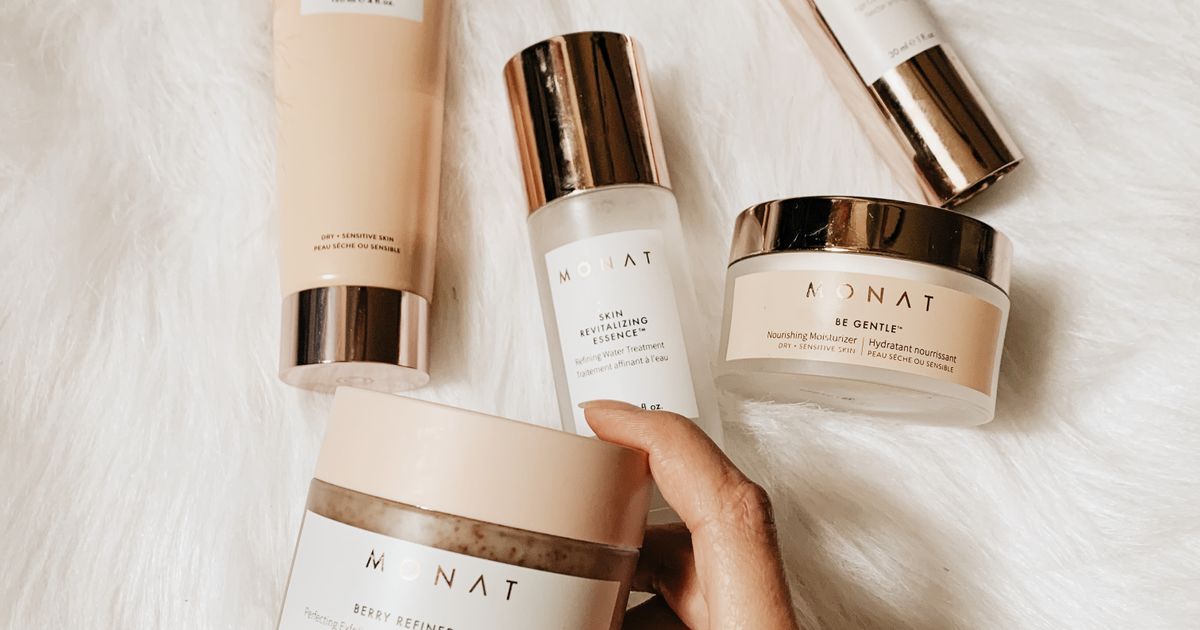 Skincare products with gold caps arranged on a white surface with a hand reaching for one