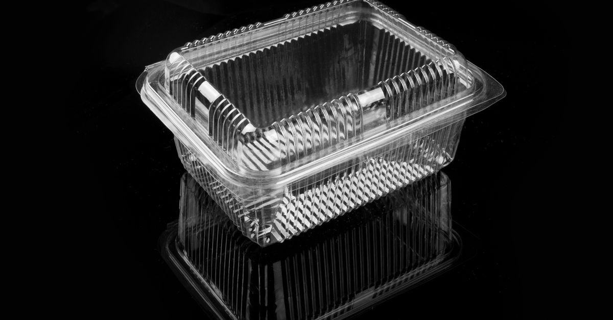 Recipiente de plástico transparente para alimentos sobre uma superfície preta refletora, estilo minimalista.