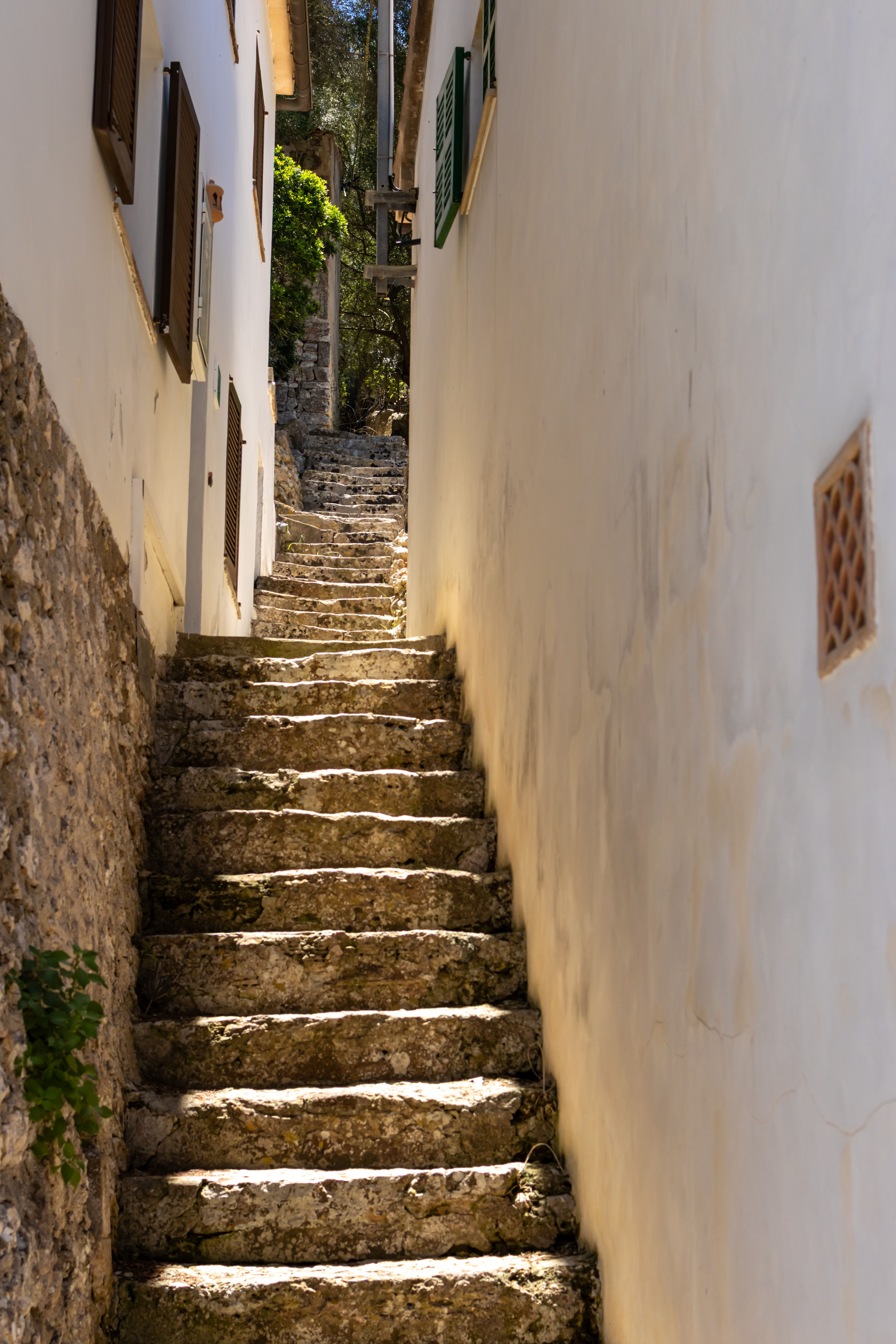 A narrow, rustic stone alleyway between buildings in Spain, bathed in sunlight.