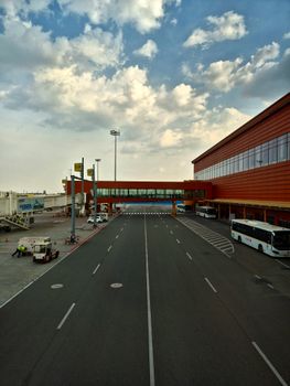 A bustling airport tarmac with terminal and buses under a cloudy sky.