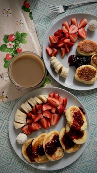 Plates of syrniki with strawberries, bananas, and coffee for a perfect breakfast start.