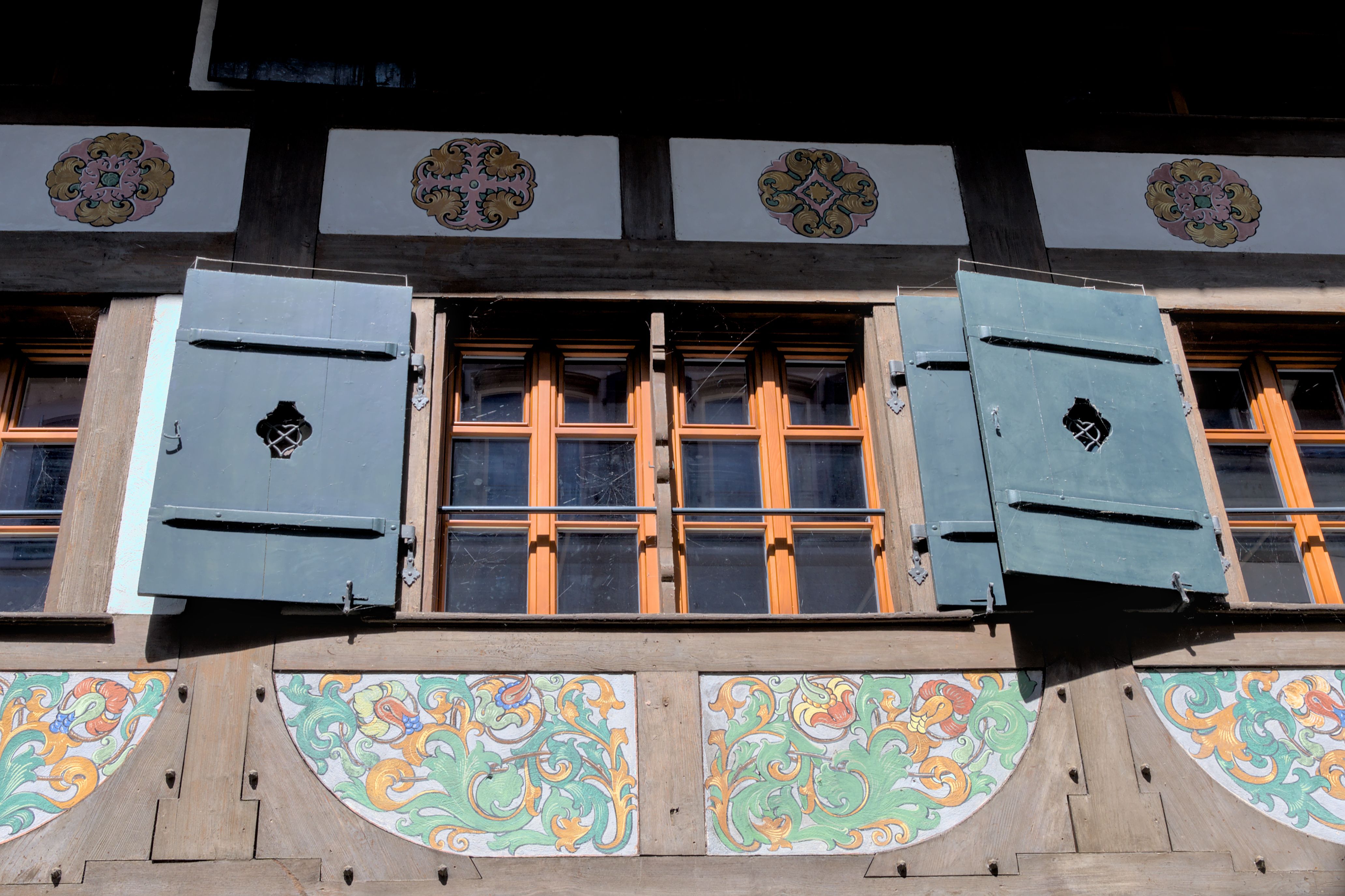 Close-up of a Swiss building's windows with decorative shutters and vibrant patterns.