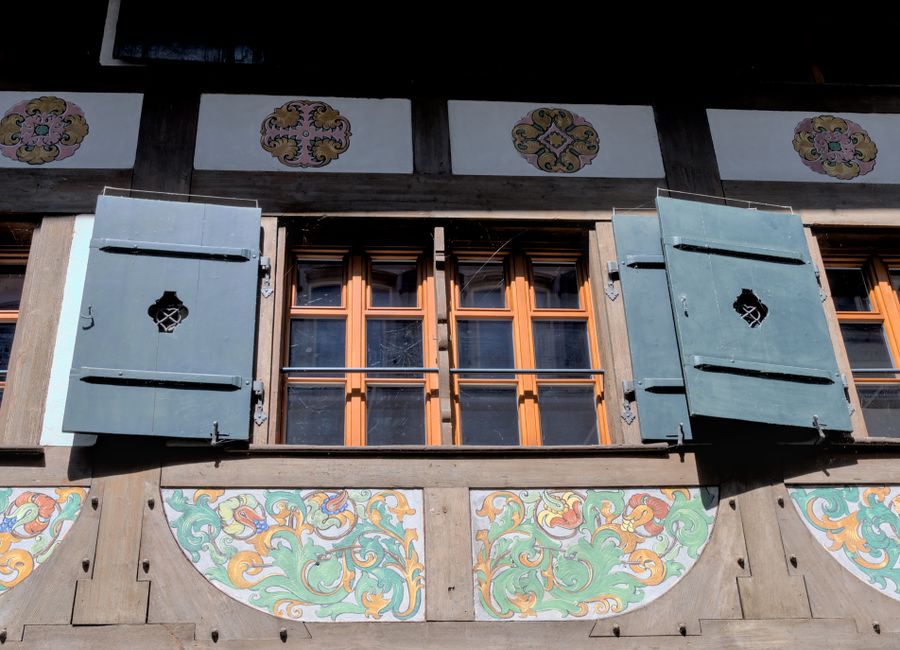 Close-up of a Swiss building's windows with decorative shutters and vibrant patterns.