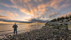 Man Standing on Rocky Shore during Sunset