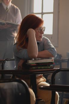 A thoughtful student sitting in a classroom, surrounded by books, during the day.