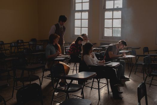 Group of students studying in a dimly lit classroom with vintage desks and natural light.