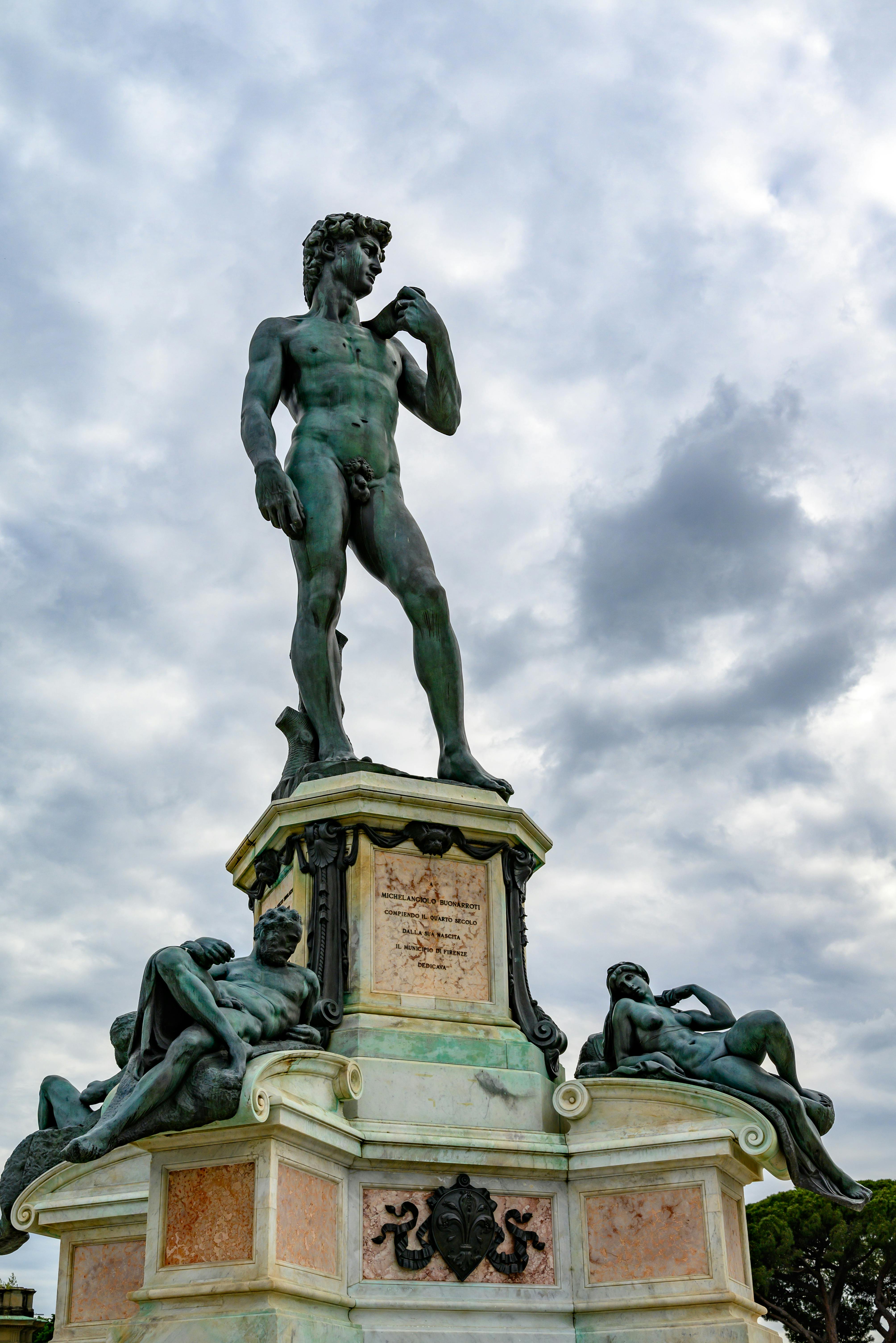 Bronze replica of Michelangelo's David statue against a cloudy sky in Florence, Italy.