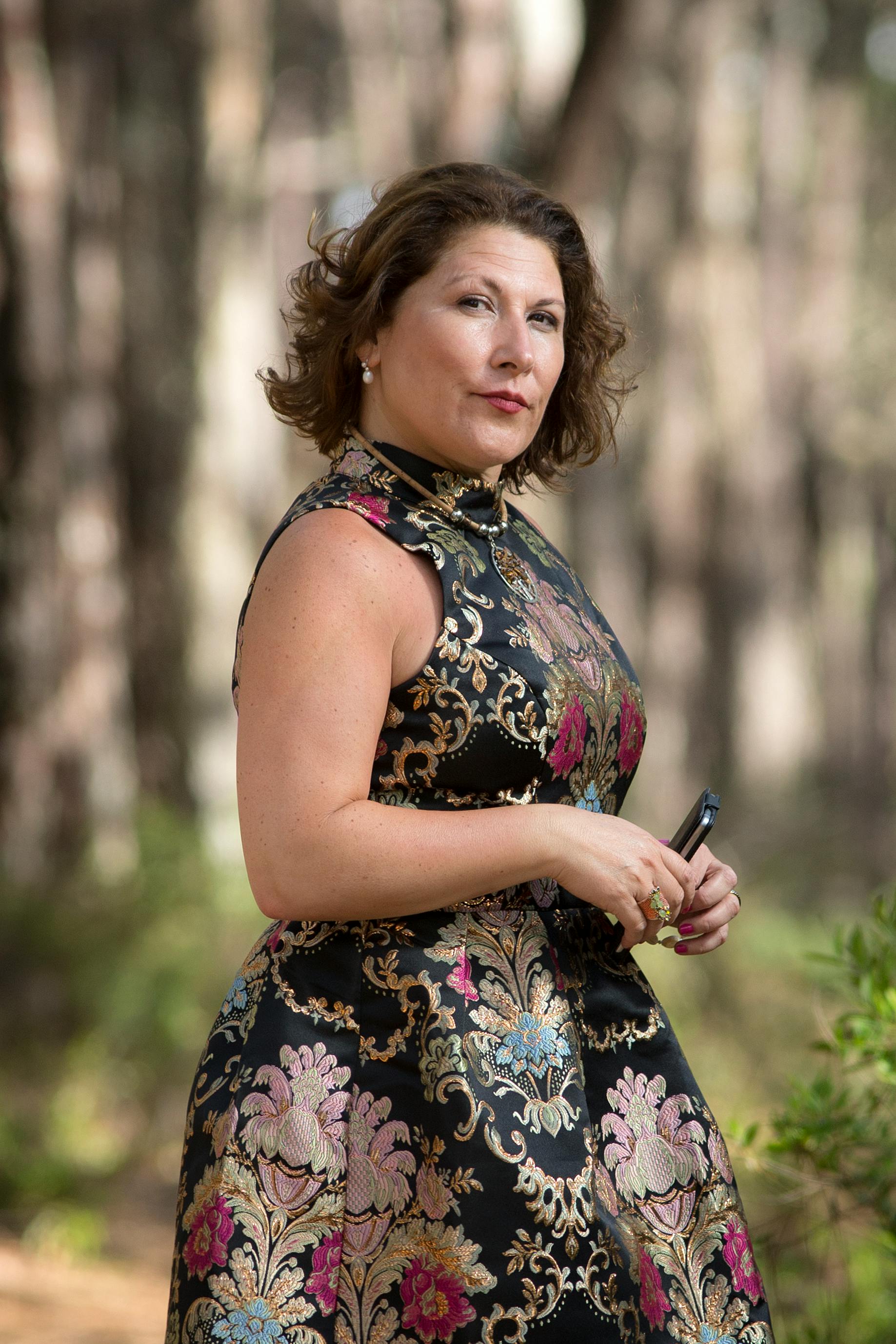 Woman in floral dress elegantly posing in a serene forest setting.