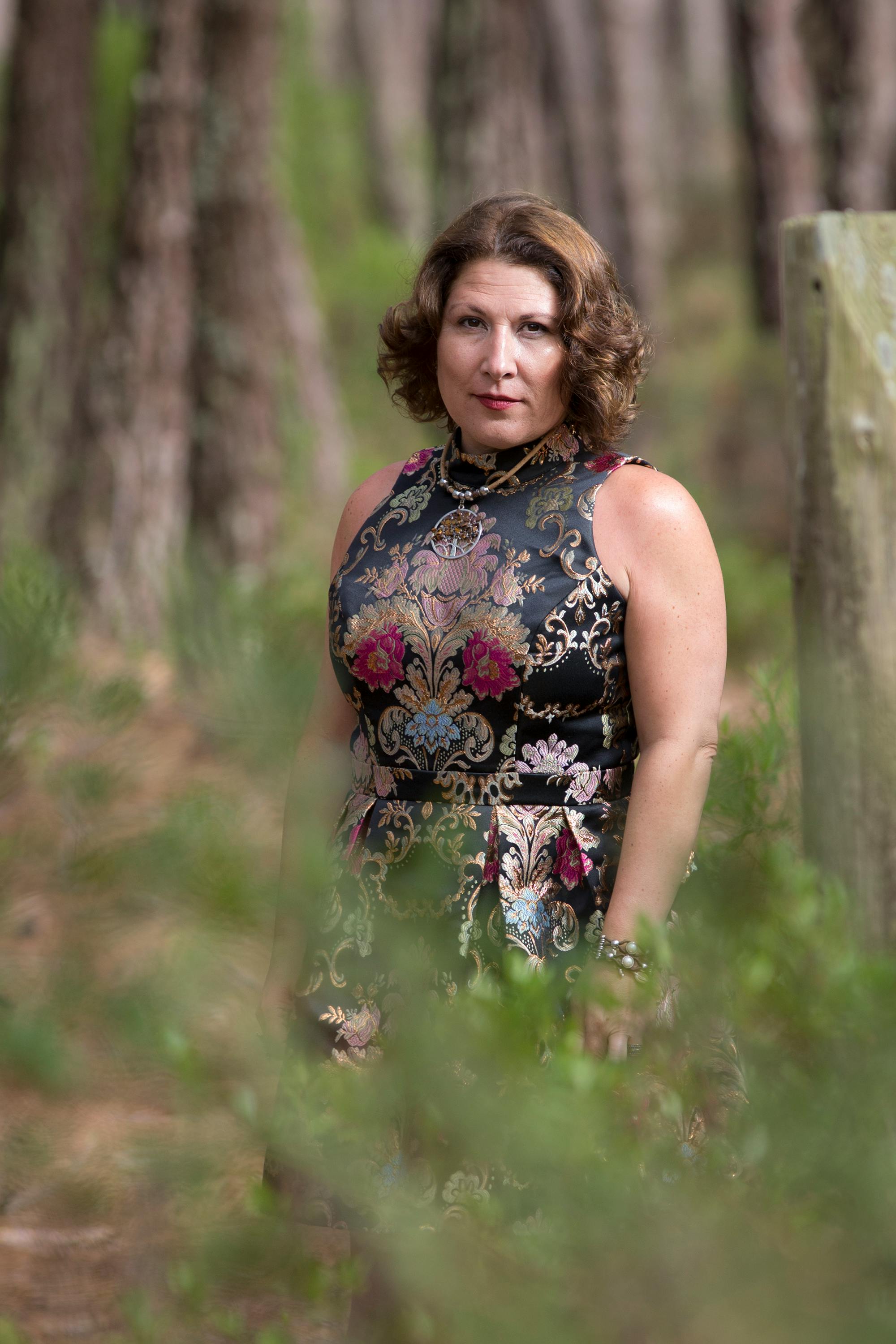 A woman in a floral dress stands gracefully in a sunlit forest scene.