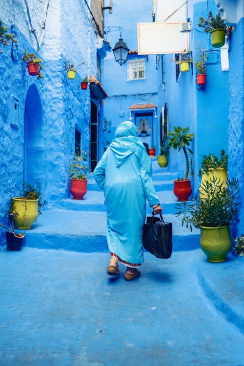 Free A person walks through the iconic blue-painted alley in Chefchaouen, Morocco, surrounded by colorful potted plants. Stock Photo