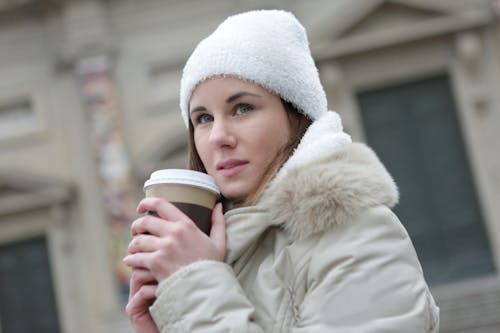 Woman in White Jacket Holding White Disposable Cup