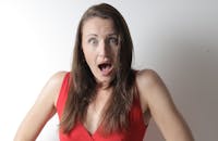 一名身穿红色上衣的年轻女子在室内面对镜头，脸上露出惊讶的表情