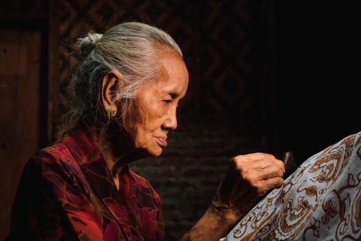 Senior woman focused on creating intricate traditional Batik design, highlighting cultural craftsmanship.