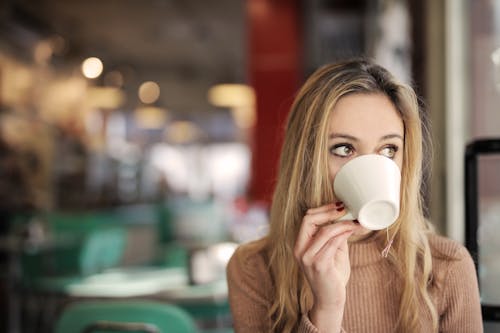 Free Woman In Brown Long Sleeve Drinking On White Ceramic Mug Stock Photo