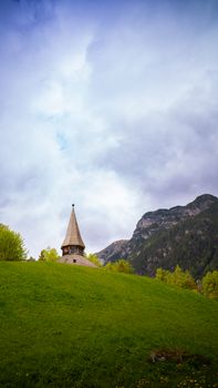 A picturesque church spire amidst lush green meadows and mountains in Trins, Tyrol, Austria.