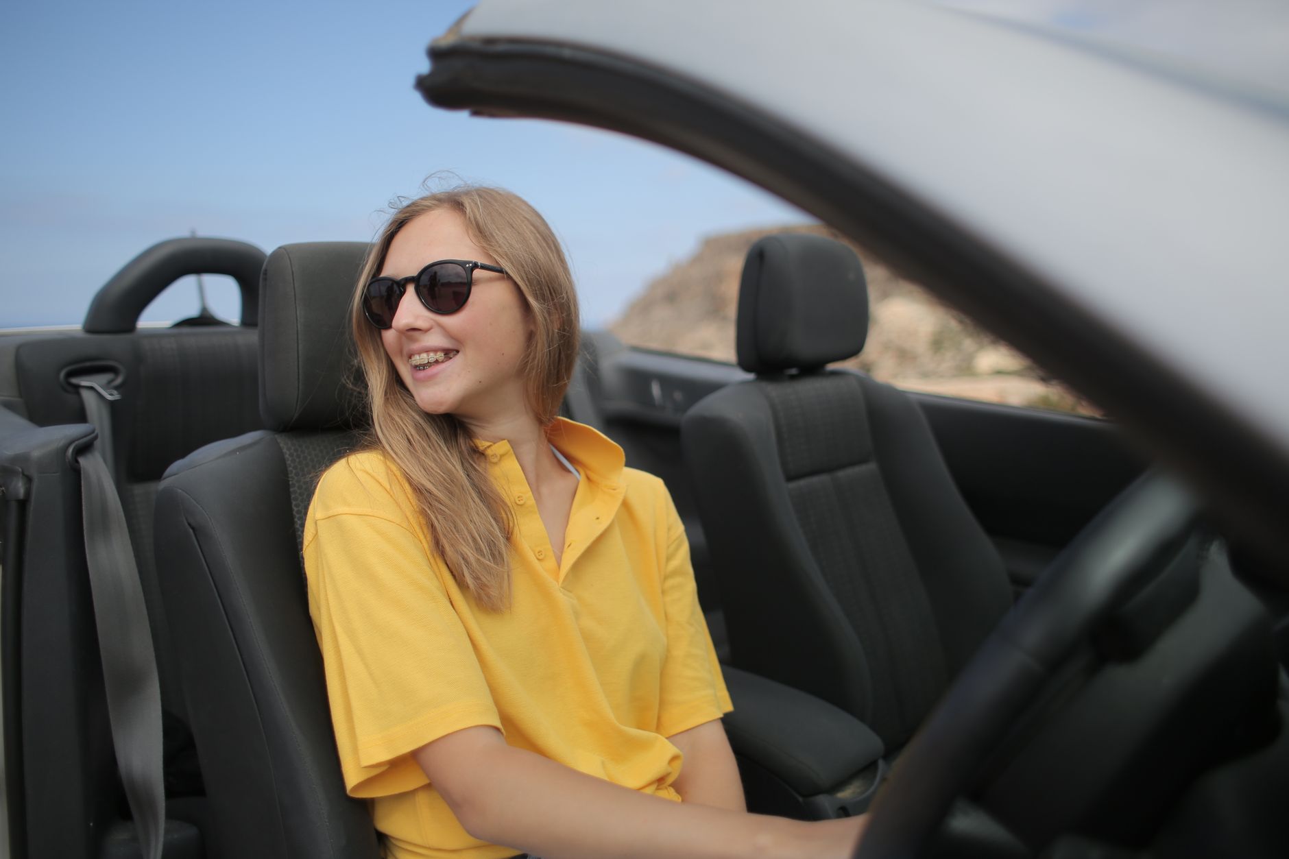 Glunderende vrouw met zonnebril in een cabriolet, genietend van een zonnige rit.
