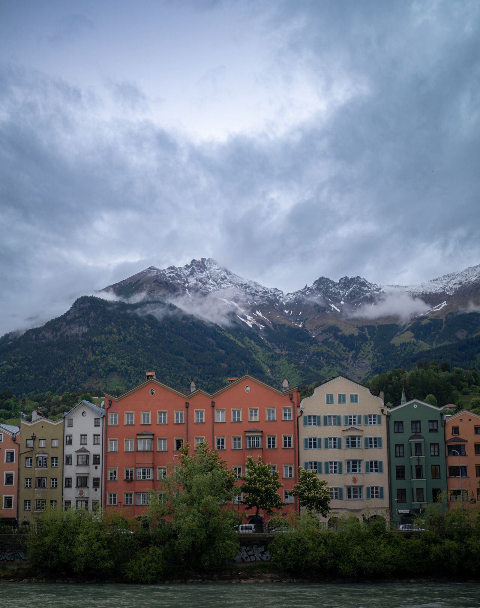 Colorful historic houses lining the Inn River in Innsbruck beneath forested mountains