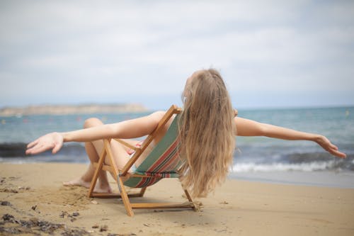 Woman in Blue and Brown Bikini Sitting on Brown Wooden Folding Chair on Beach