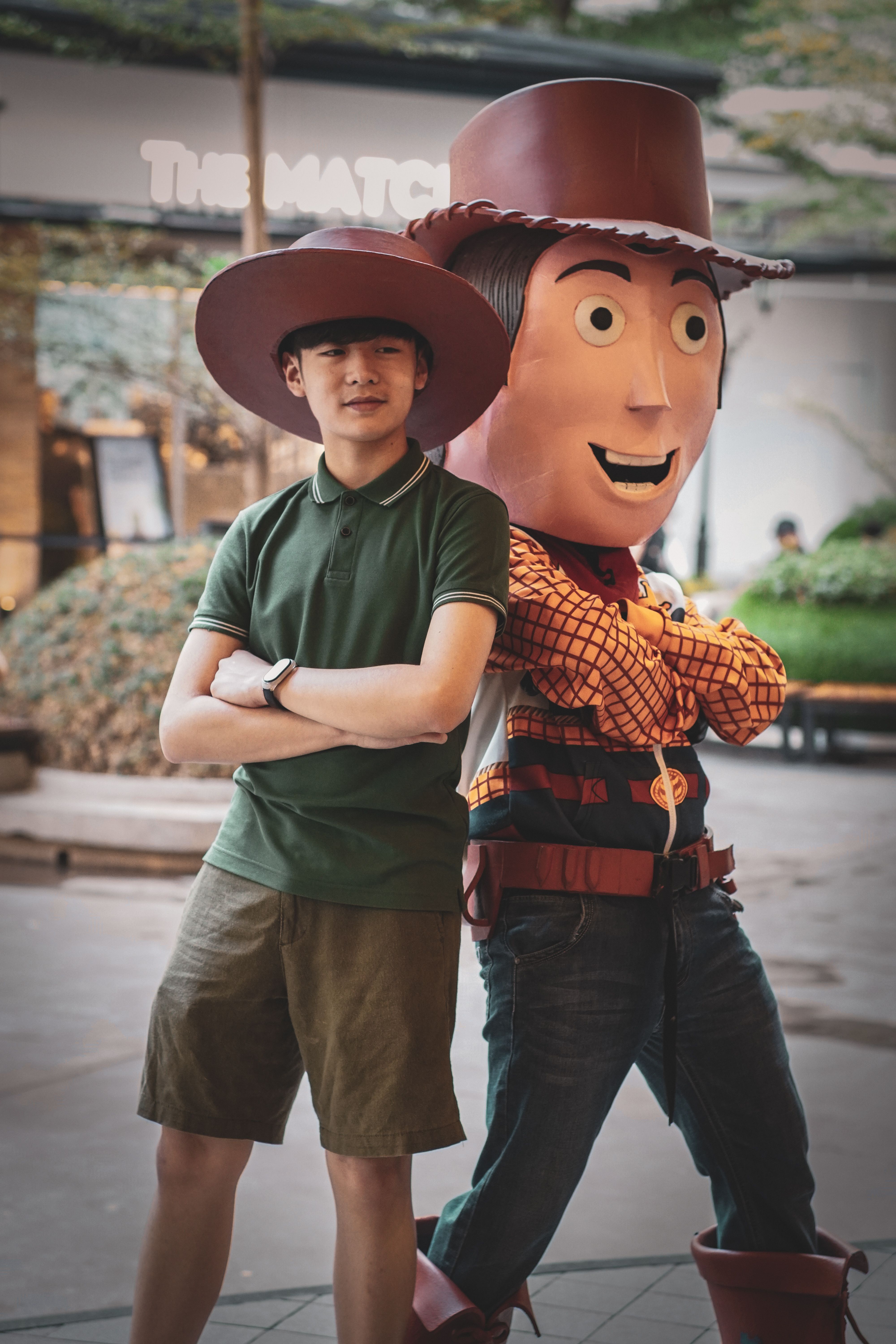 A teenager poses with a costumed cowboy character in an outdoor setting, conveying a playful and fun mood.