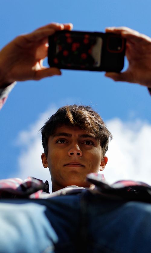 Free Young man capturing a selfie with a smartphone against a clear blue sky. Stock Photo