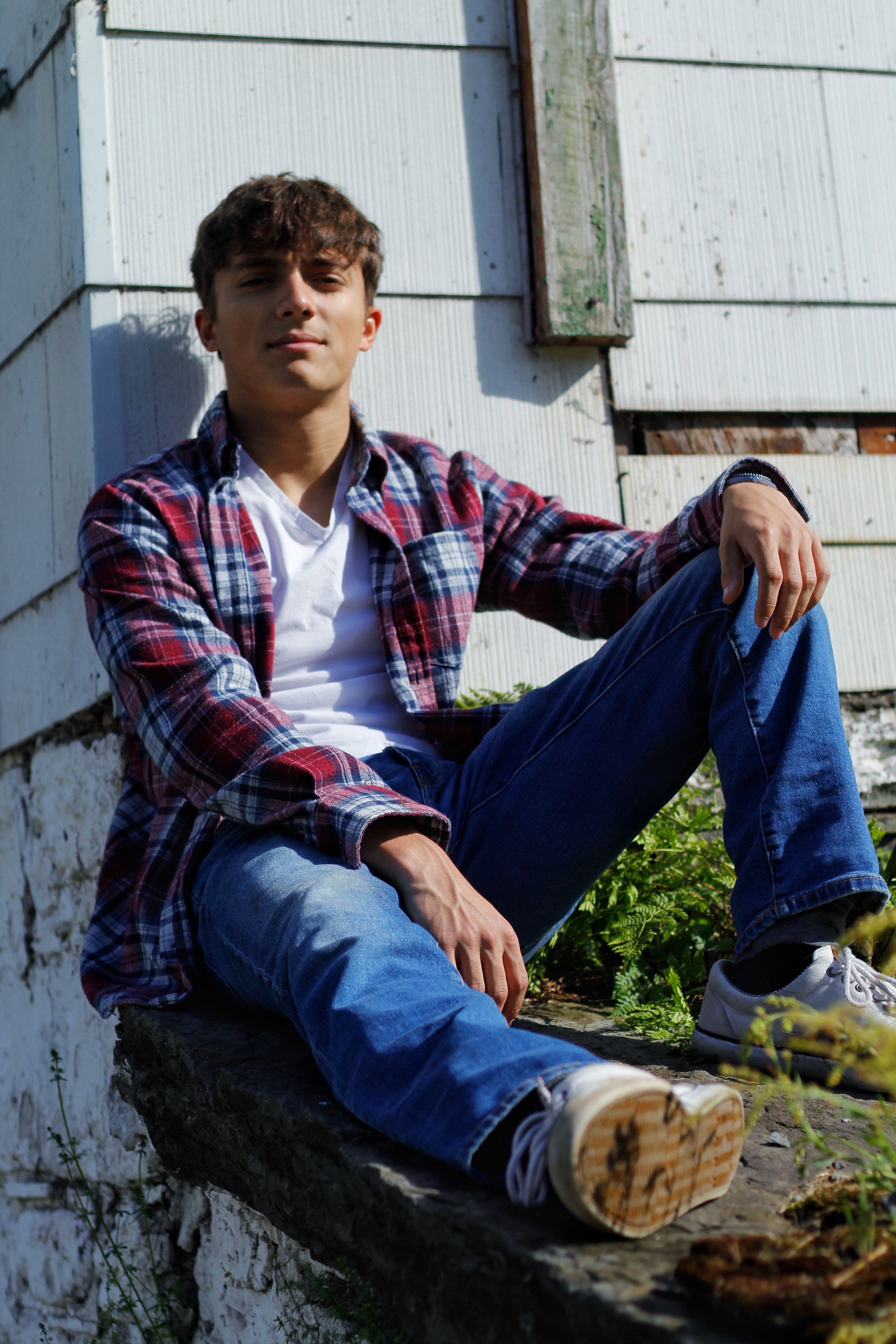Young man in casual attire sitting outdoors against a rustic wall.