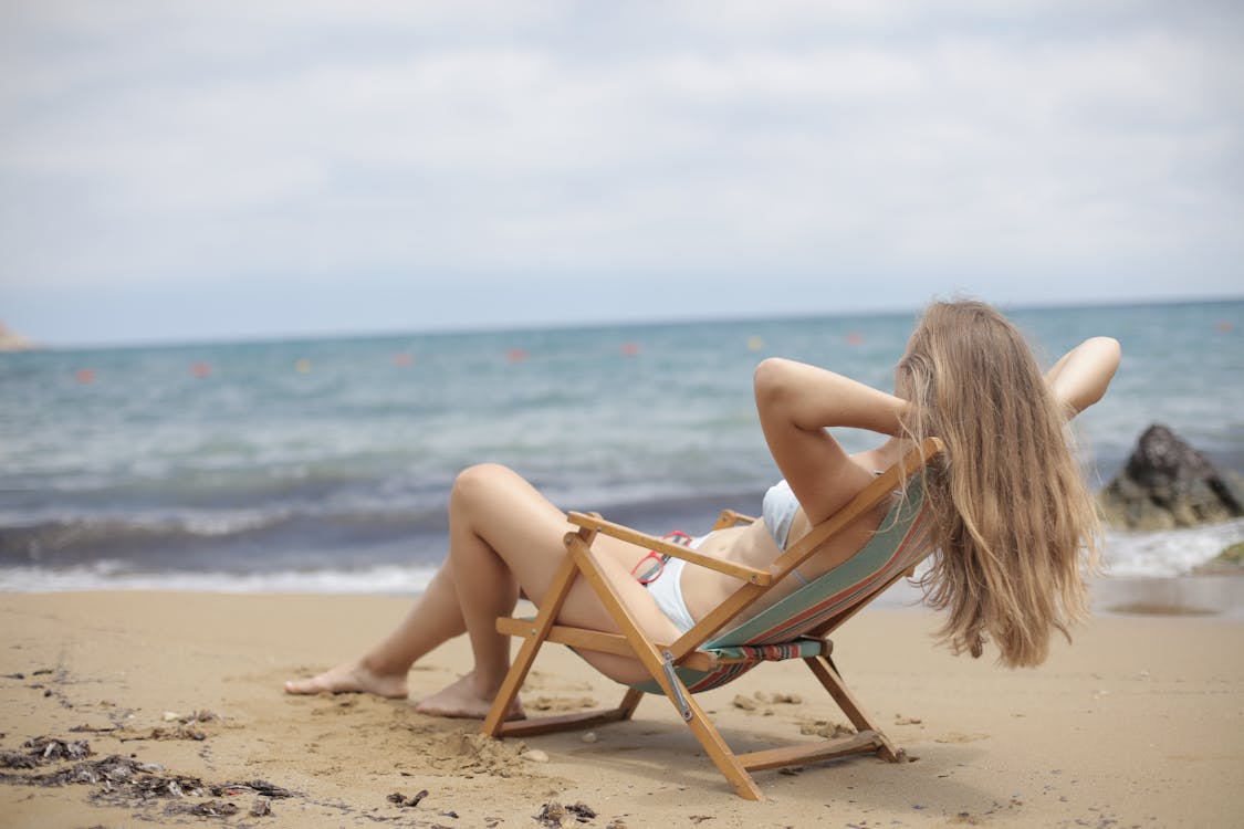 Woman in Blue Bikini Sitting on Brown Wooden Folding Chair on Beach