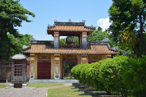 Free Historic Vietnamese architectural gate surrounded by lush garden foliage under a clear blue sky. Stock Photo
