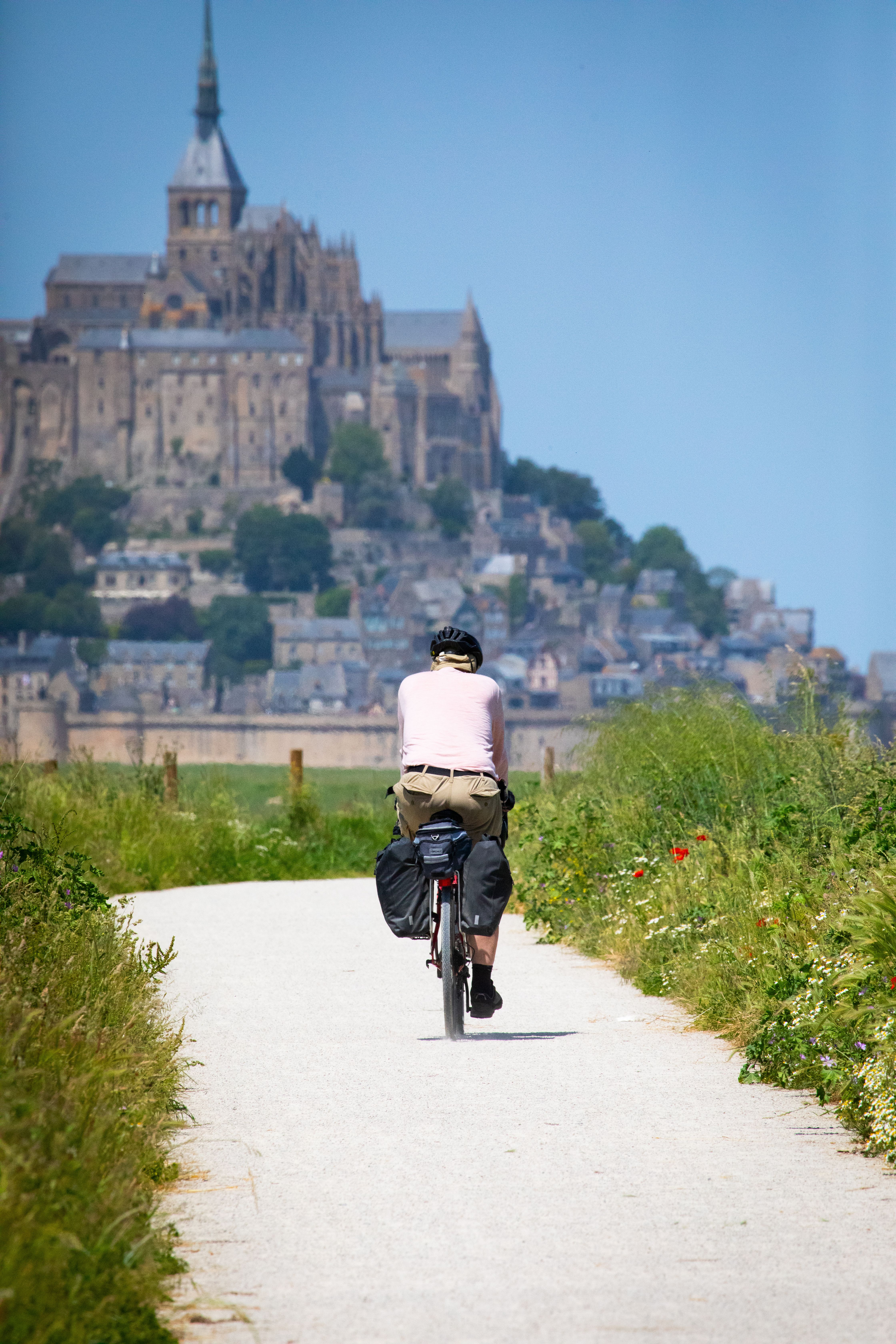Kostnadsfria En cyklist cyklar mot den historiska Mont Saint-Michel i Normandie, Frankrike, på en solig dag. Stock foto