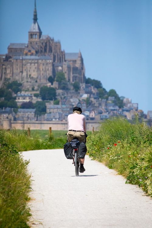 Kostnadsfria En cyklist cyklar mot den historiska Mont Saint-Michel i Normandie, Frankrike, på en solig dag. Stock foto