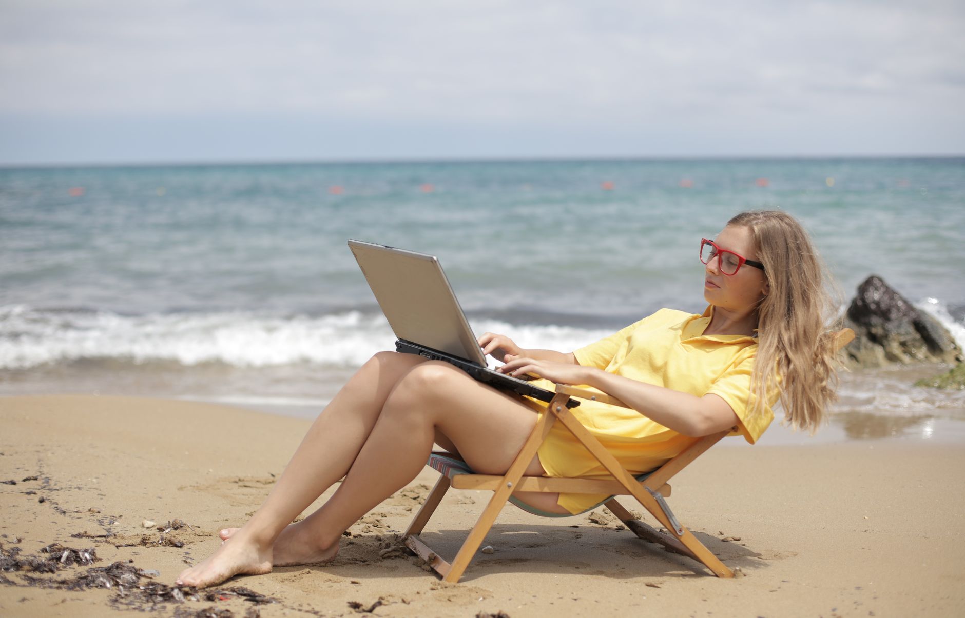 Woman relaxing on beach chair while using laptop - remote work lifestyle
