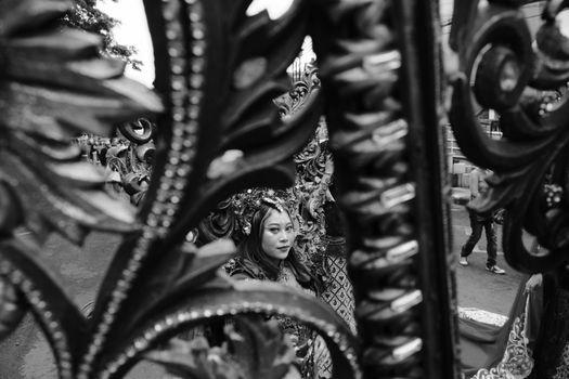 A woman in traditional attire at a festival in Bandung, captured through ornate ironwork.