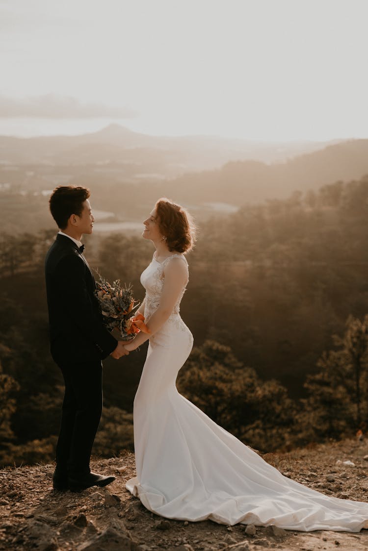 Man In Black Suit And Woman In White Wedding Dress Holding Hands Facing Each-other