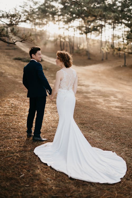 Woman in White Wedding Gown Holding Hands with Man in Black Suit