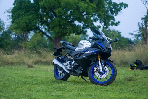 Free A sleek black and blue motorcycle parked on grassy terrain surrounded by lush trees. Stock Photo