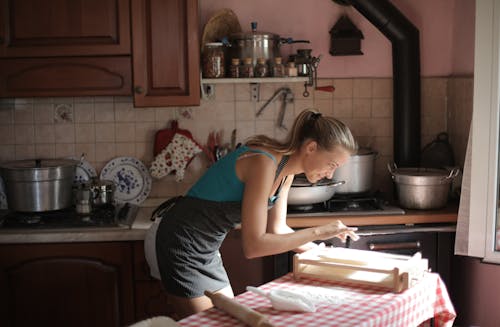 Женщина в синей майке стоит возле кухонной стойки