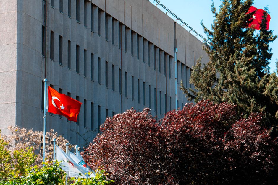 Modern government building in Ankara with Turkish flag and lush trees.