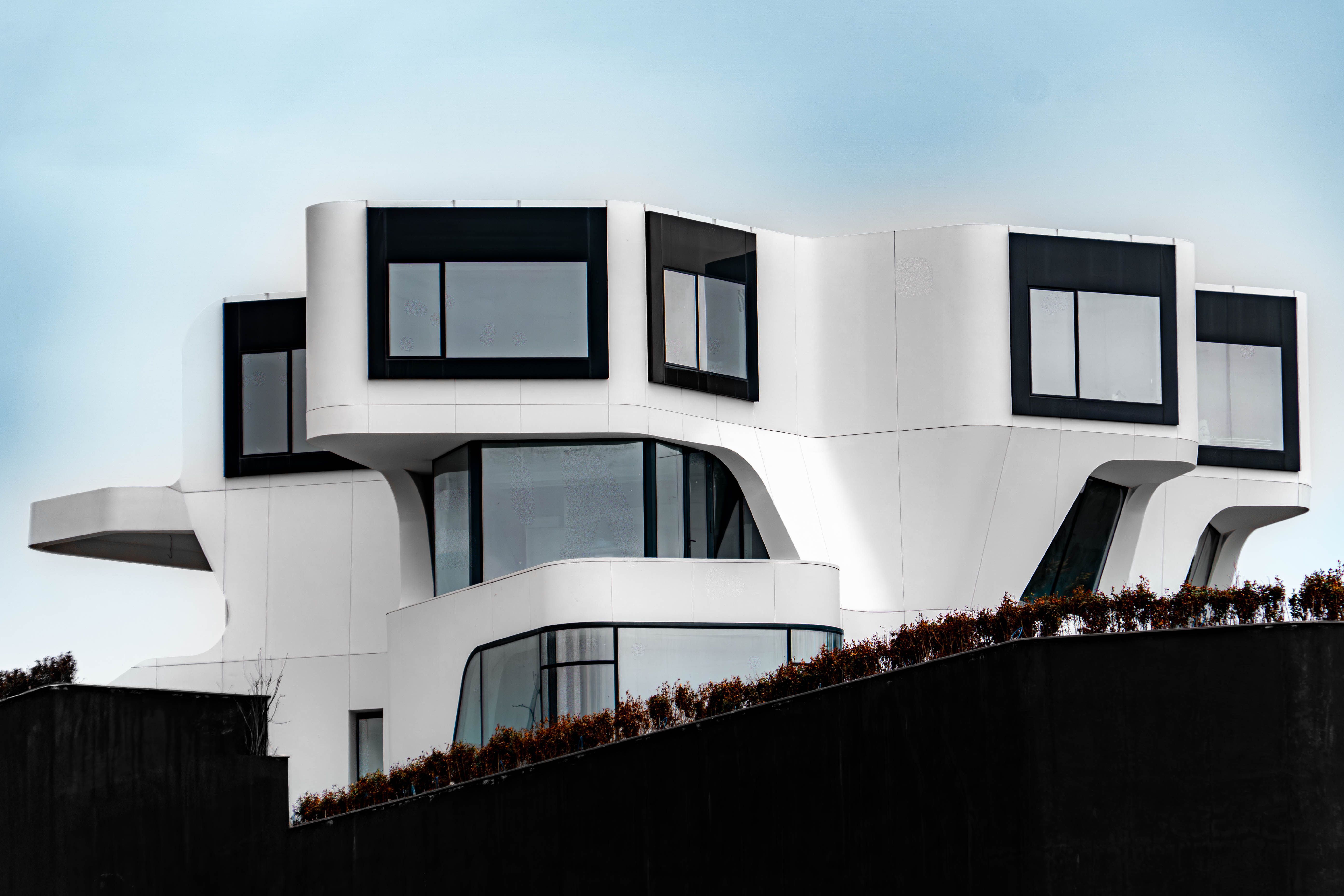 Modern white house with black-framed windows on a sloped hillside under a pale sky
