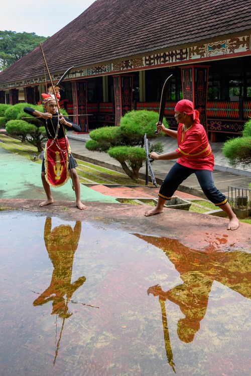 Free Two men in traditional attire engage in Indonesian martial arts outside a cultural building. Stock Photo