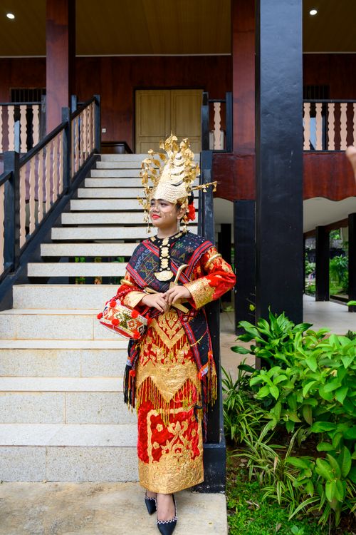 Free A woman dressed in vibrant traditional Sumatra wedding attire stands before a staircase, showcasing cultural heritage. Stock Photo