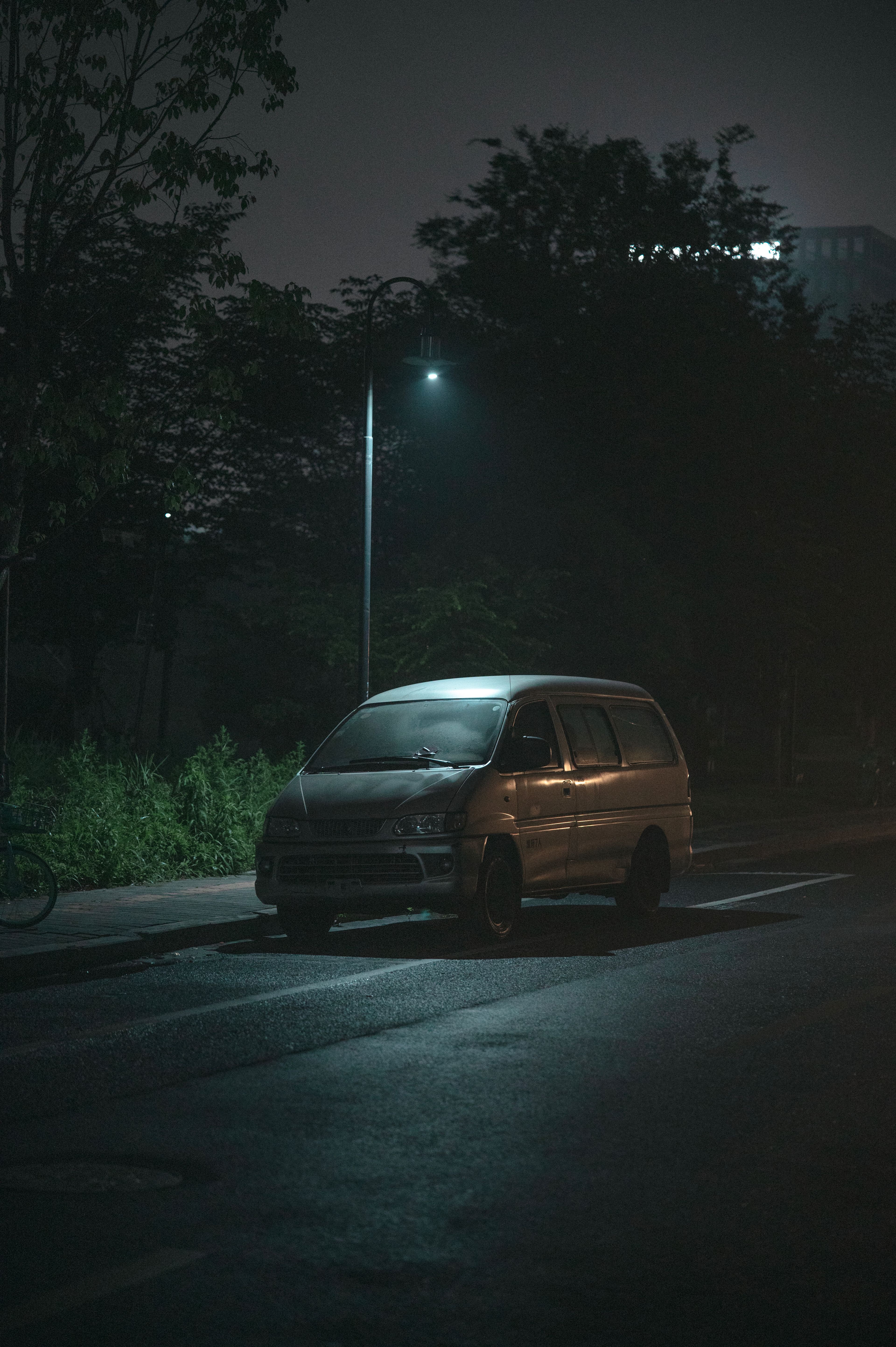 Véhicule utilitaire sans marquage stationné sous un lampadaire, de nuit, dans une rue déserte.