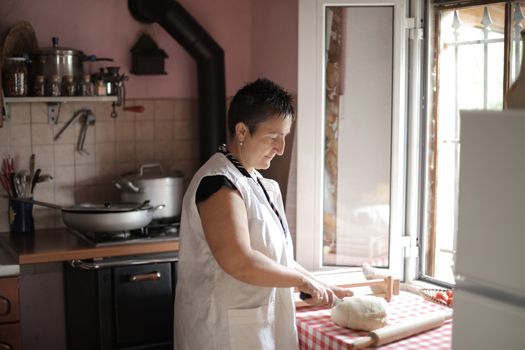 Middle-aged woman slicing dough on a kitchen counter with natural light.