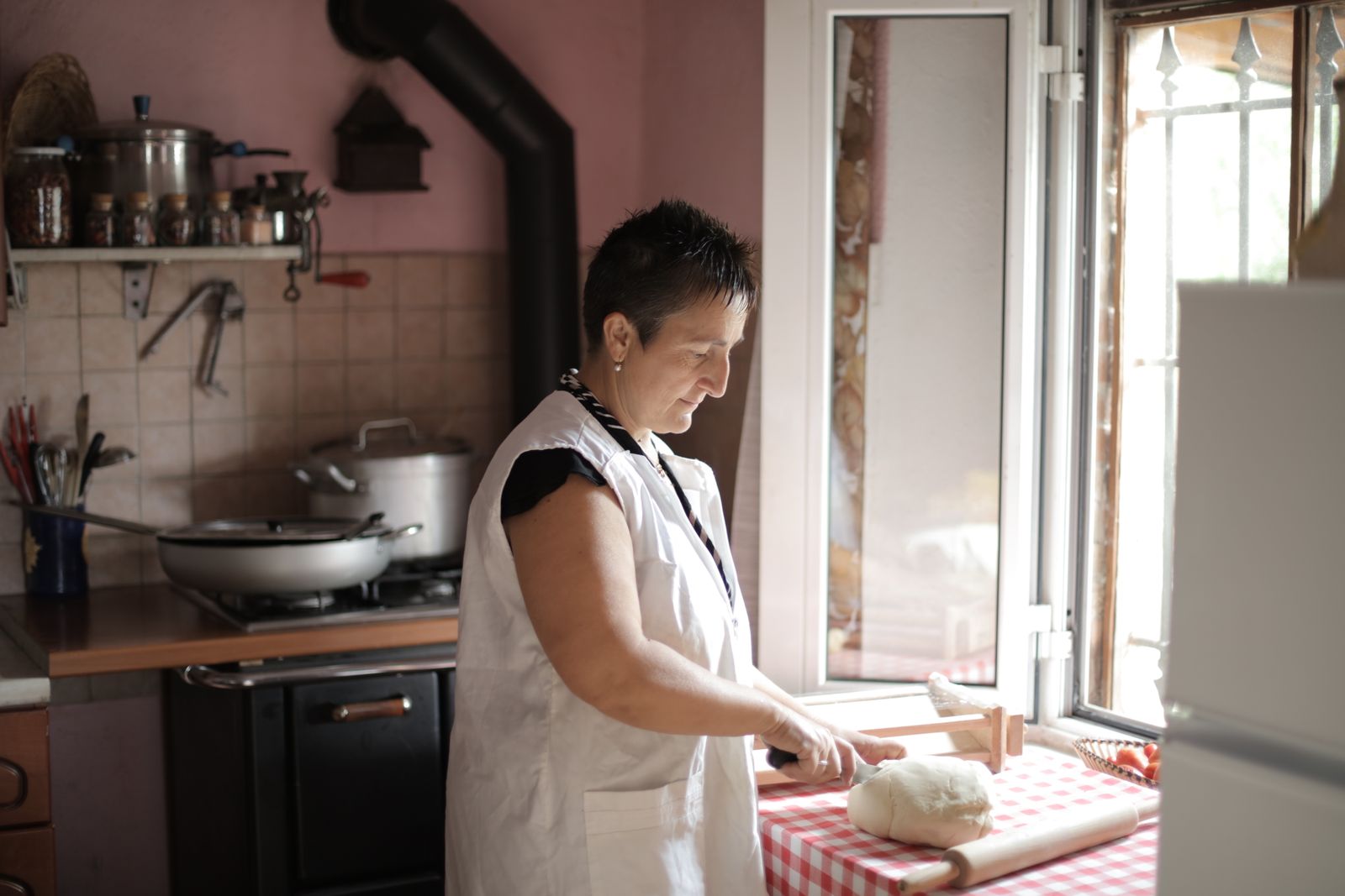 Middle-aged woman slicing dough on a kitchen counter with natural light.