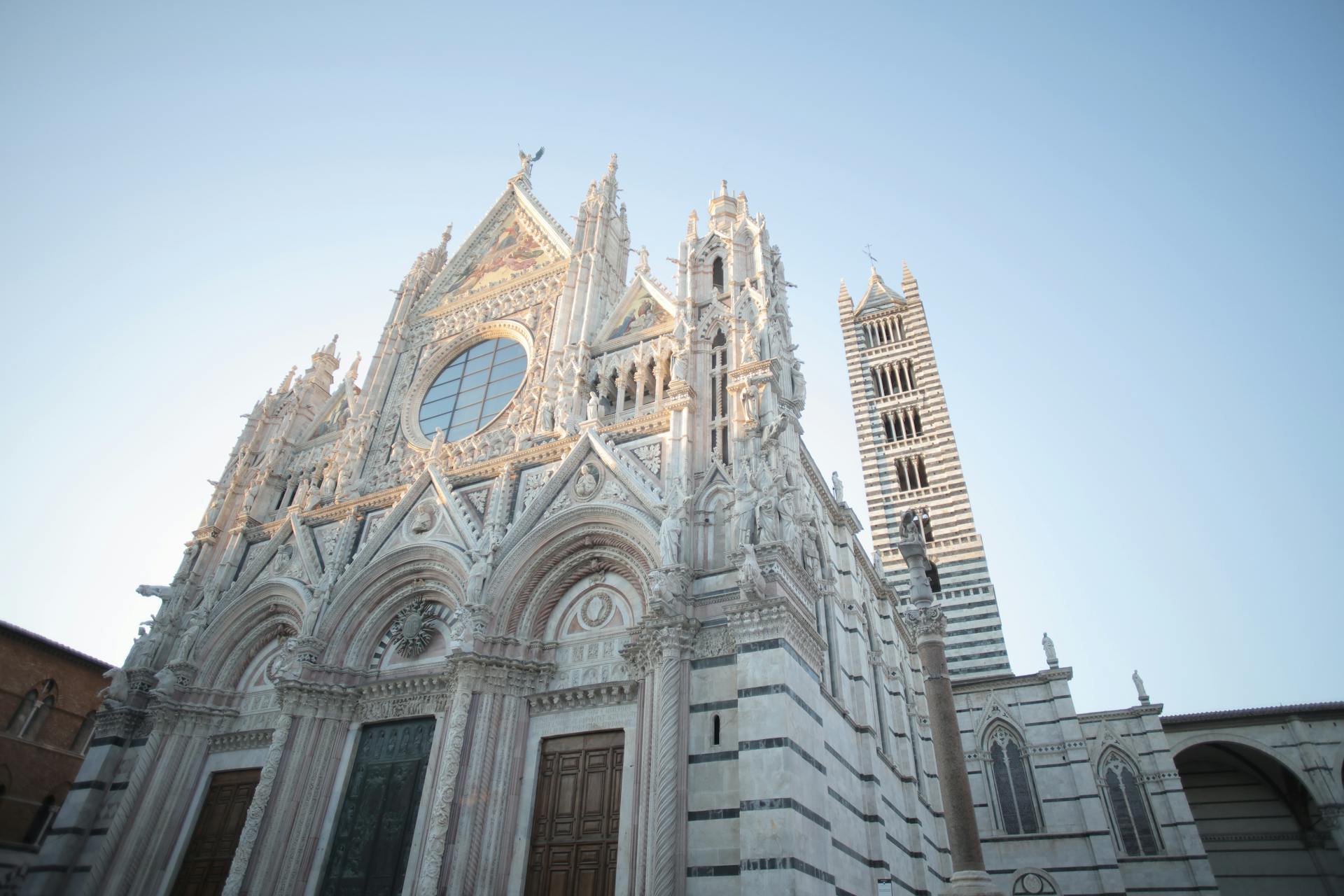 Magnificent low angle photo of Siena Cathedral's gothic facade in Italy under clear blue sky.